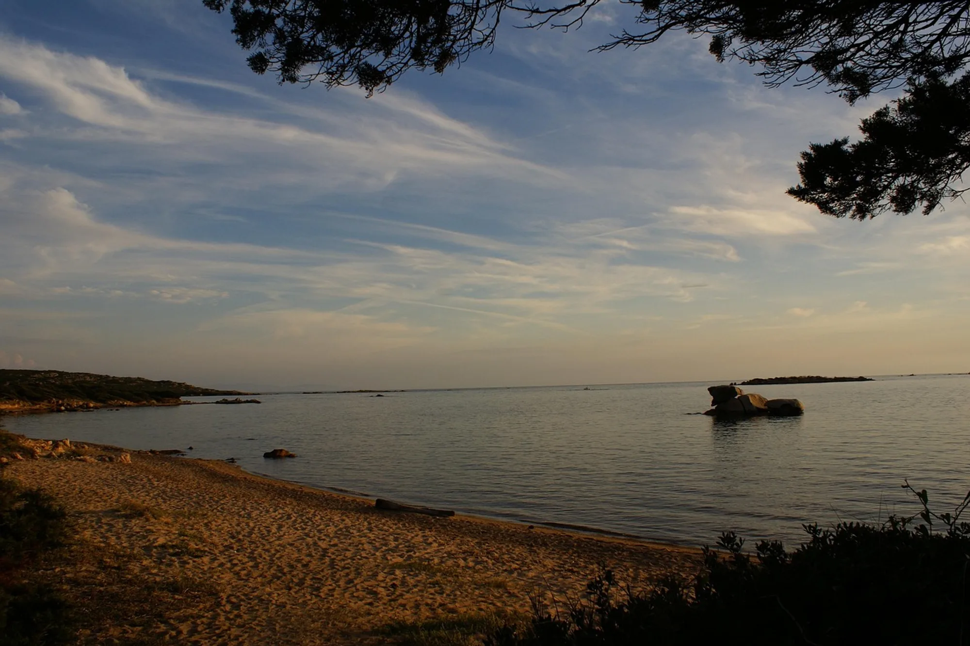 Une plage de sable de Figari au soir, un rocher isolé dans l’eau calme