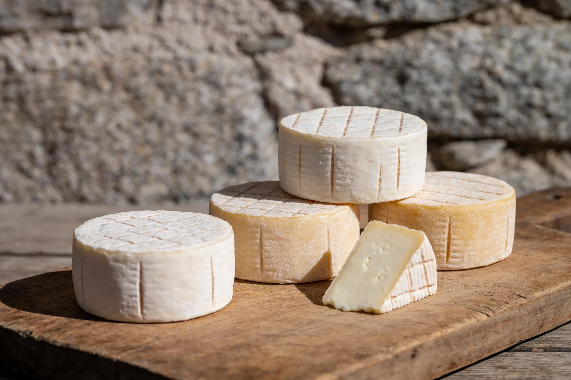 Petites tommes fermières de brebis à croûte naturelle, sur une planche en bois devant un mur de granit