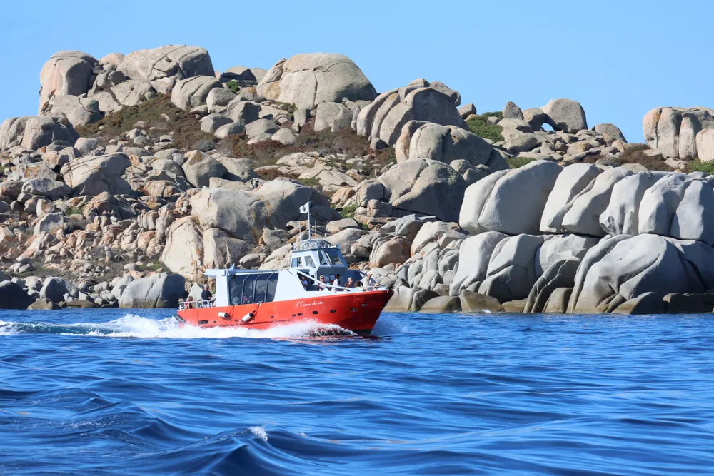Un barco de excursión bordea una costa de grandes bloques de granito