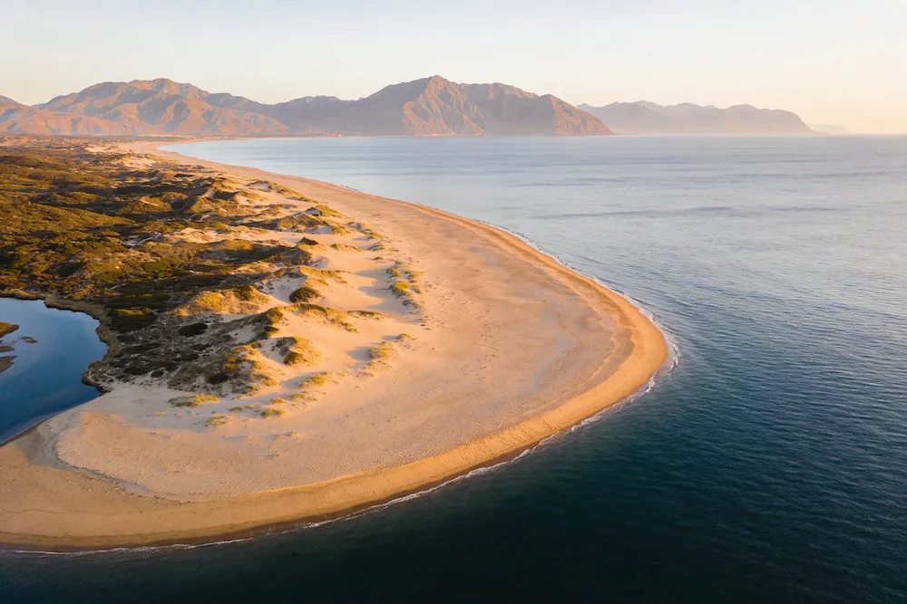 Ilustración de una playa de arena muy larga al fondo de un golfo, con dunas cerca de una desembocadura